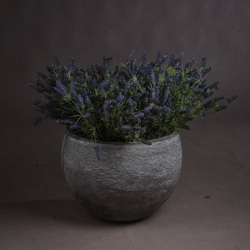A large bunch of artificial lavender arranged in a textured grey planter.