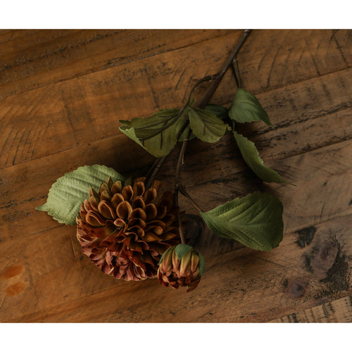 Artificial deep mustard dahlia stem with green leaves placed on a wooden surface.