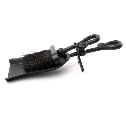 A black crook handled hearth tidy with a brush and a scoop, isolated on a white background.