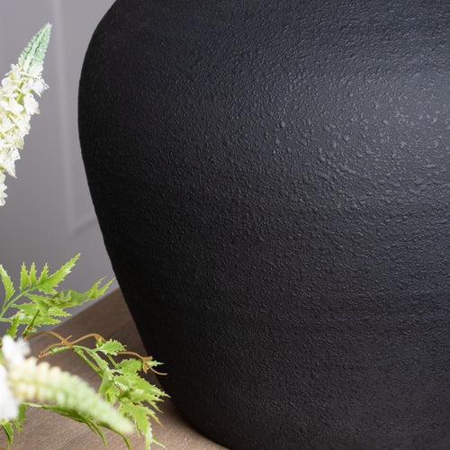 Black vase with green plants on a gray background