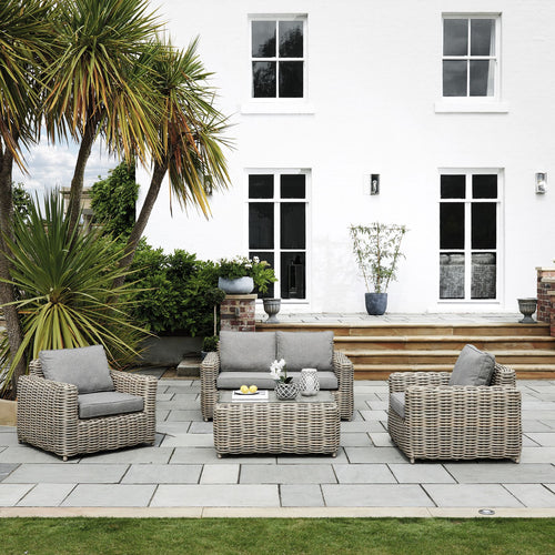 Outdoor patio set with wicker chairs and table in front of a white house.