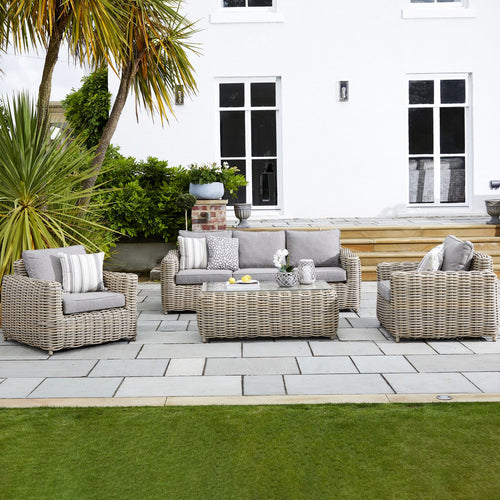 Outdoor furniture set including a sofa, loveseat, armchairs, and a coffee table made of wicker with cushions, on a stone patio.
