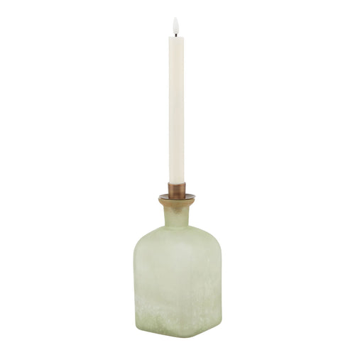 A large candle holder vase with a smoked sage green color and aged brass metal trim, with a candle placed on top.