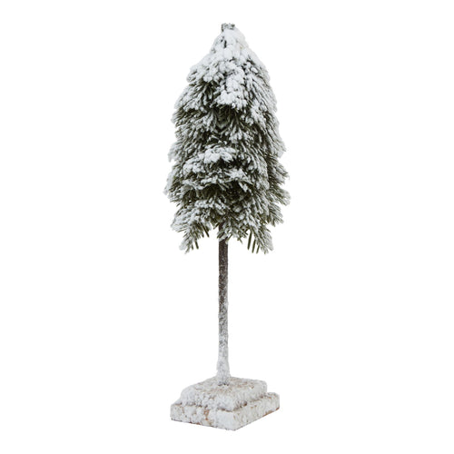 A medium-sized artificial cedar tree with snow on its branches and base, set on a rustic wood block.