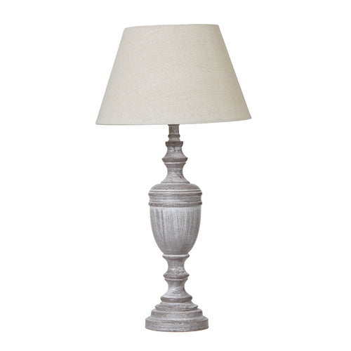 A table lamp with a linen shade and a weathered gray urn-shaped base.
