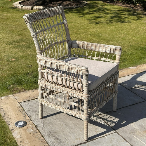Outdoor dining chair with beige rattan weave and a gray cushion, placed on a patio.