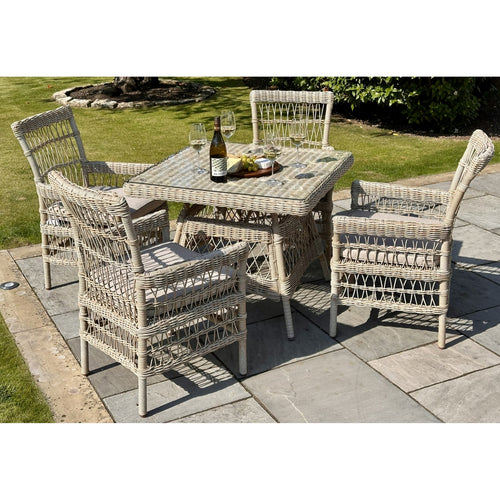 A beige 4 seater outdoor dining set made of rattan, including a square table with a glass top and four chairs, set on a patio.