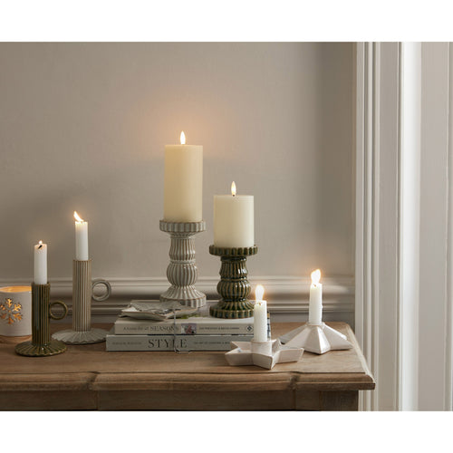 Candles in various holders on a wooden surface with a neutral background