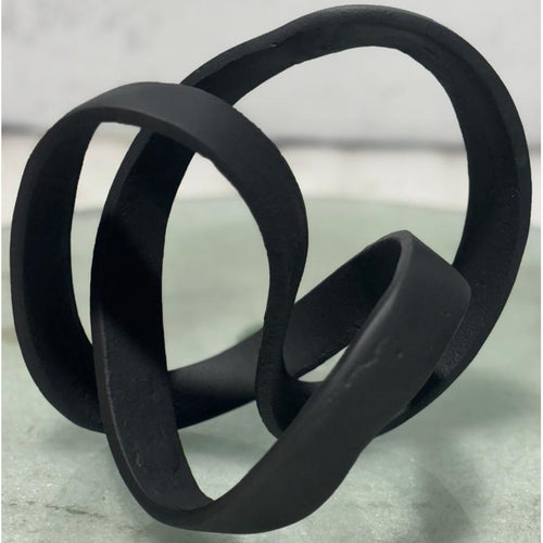 A black cast knot ornament with an intricate interplay of light and shadow through its fluid form.